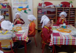 Dzieci siedzące przy dwóch stolikach spożywają kanapki z wykonaną pastą